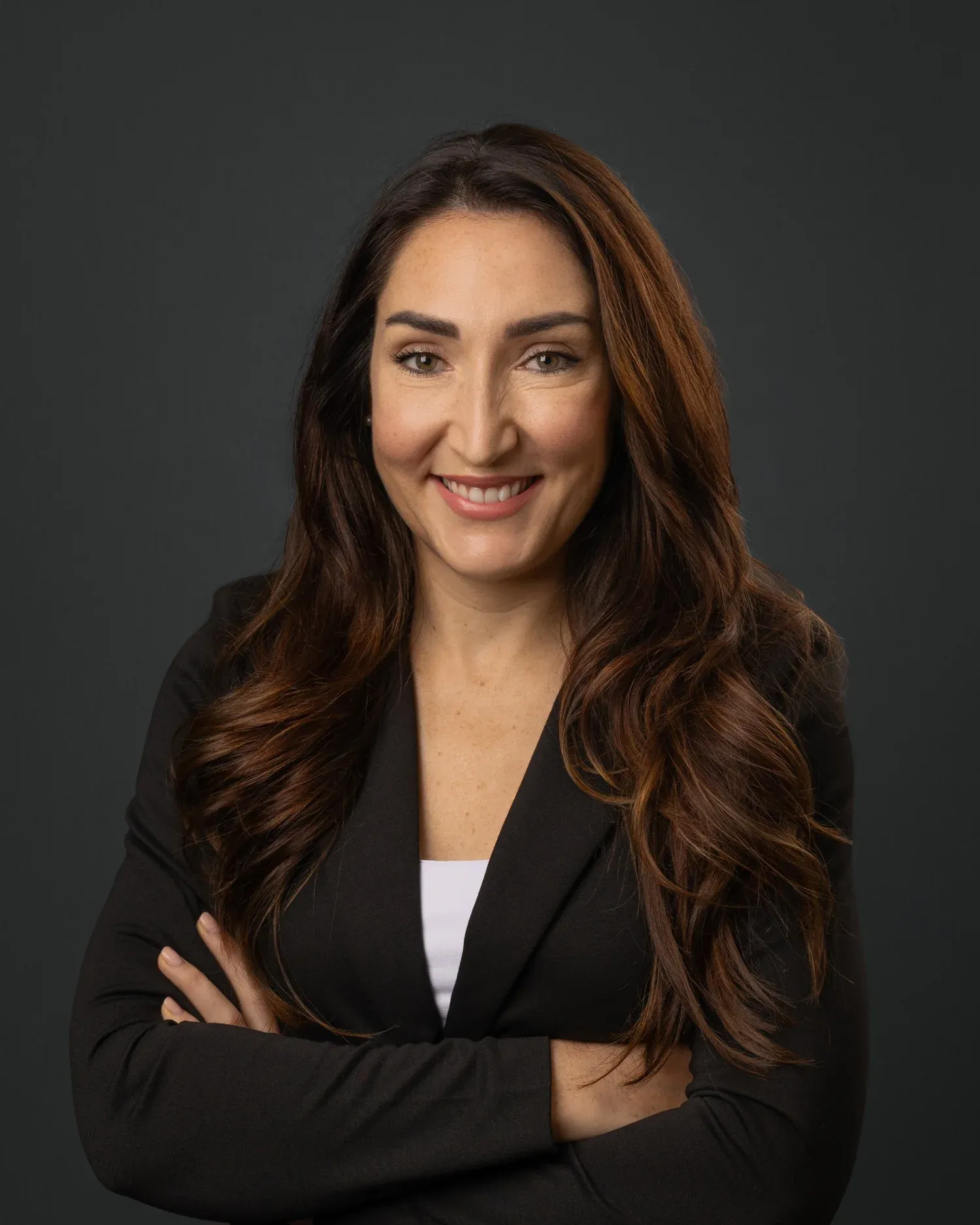 Corporate headshot of a woman with dark wavy hair in a black blazer on a grey background
