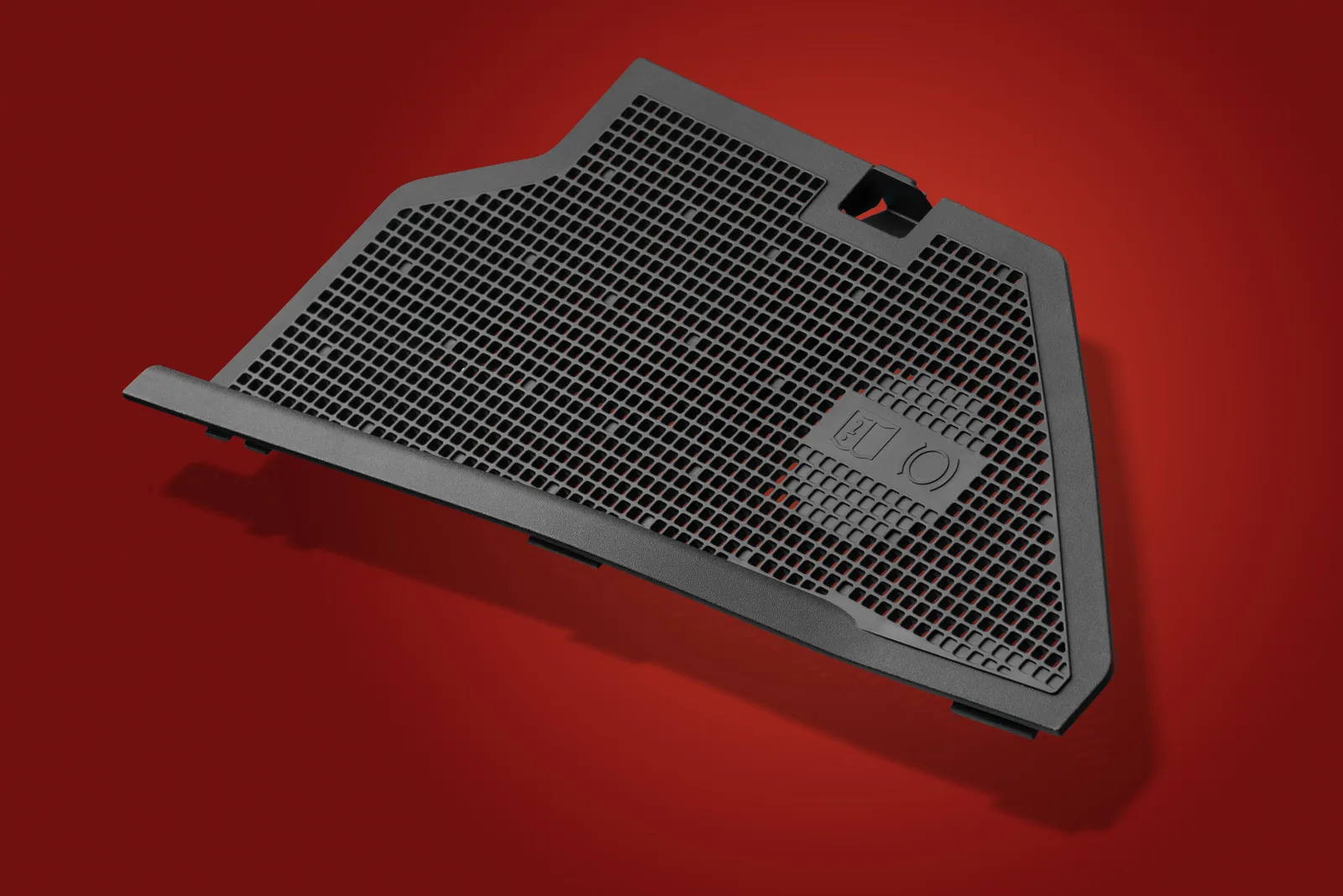 Black moulded plastic mesh panel photographed on a red studio background