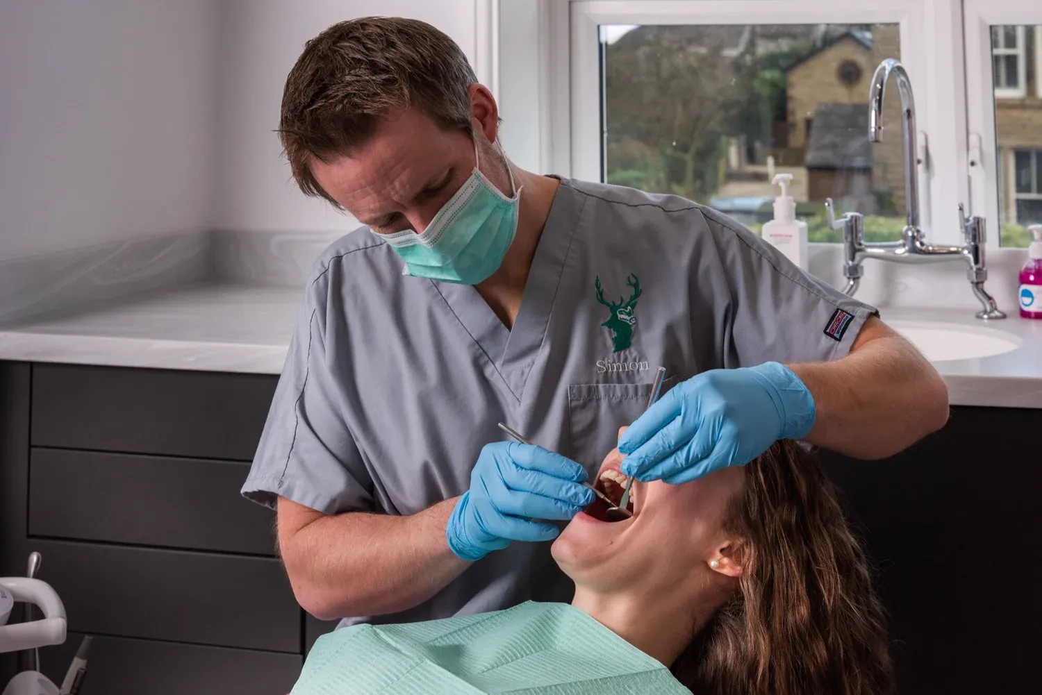 Dentist in scrubs and gloves examining a patient using dental instruments