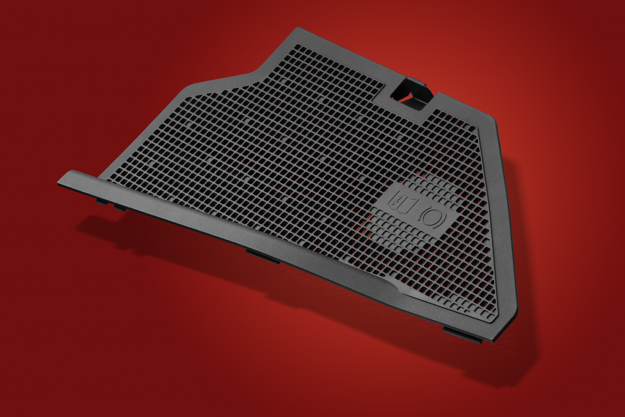Black moulded plastic mesh panel photographed on a red studio background