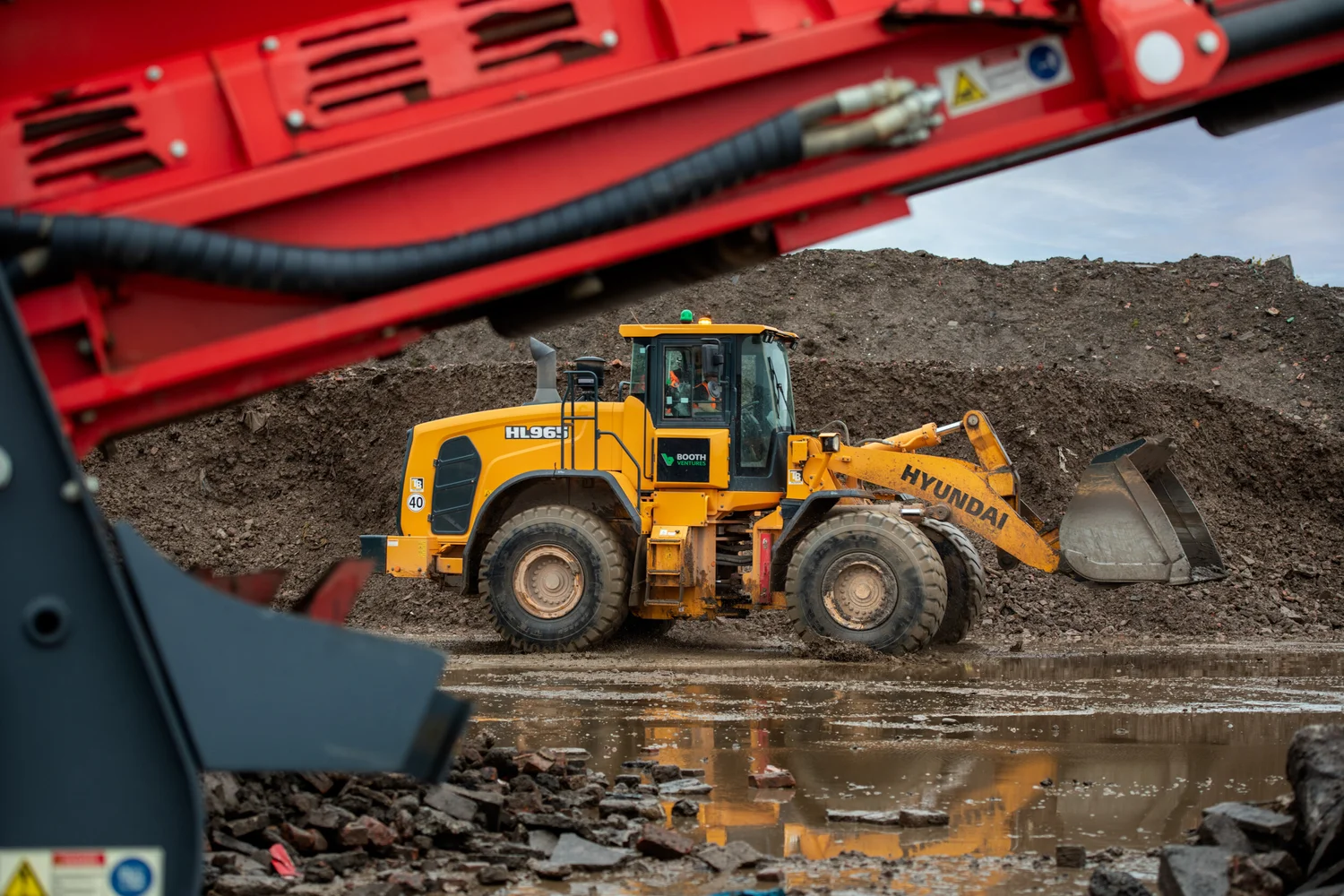 Yellow Hyundai wheel loader moving demolition rubble on a muddy recycling site