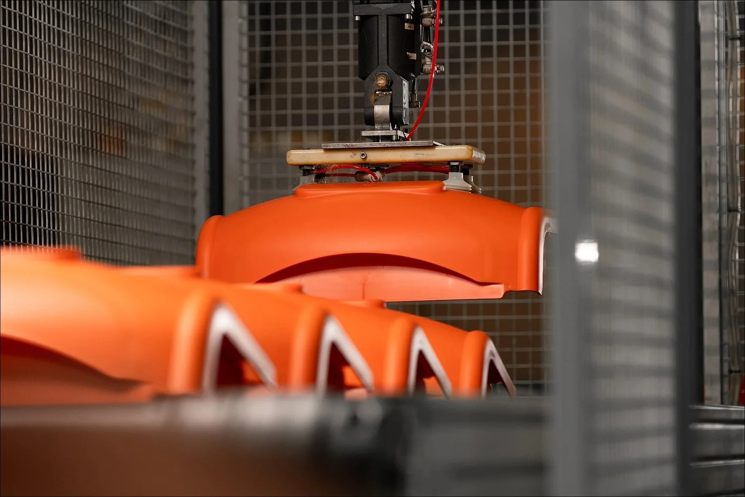 Automated pick and place robot lifting orange plastic component