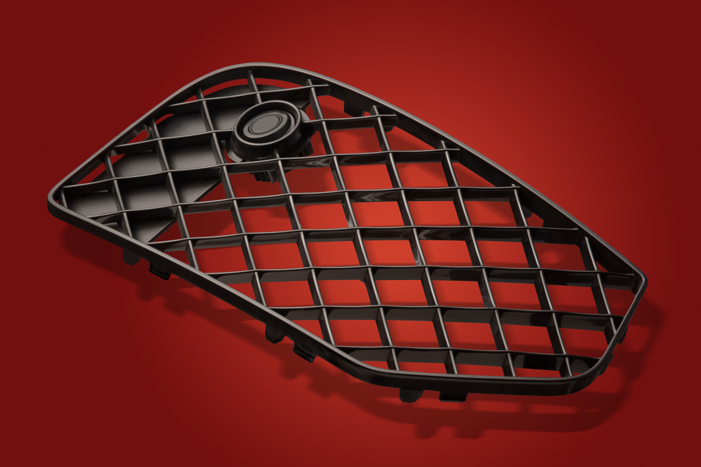 Black triangular moulded plastic grille photographed on a red studio background