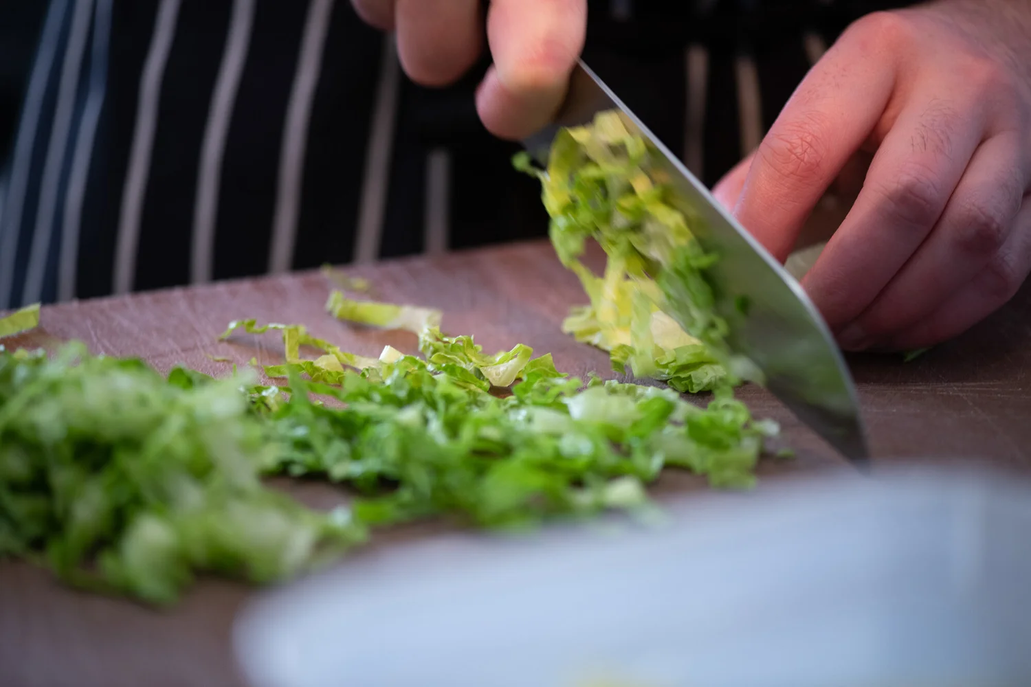 Close-up of a chef shredding lettuce with a knife on a chopping board