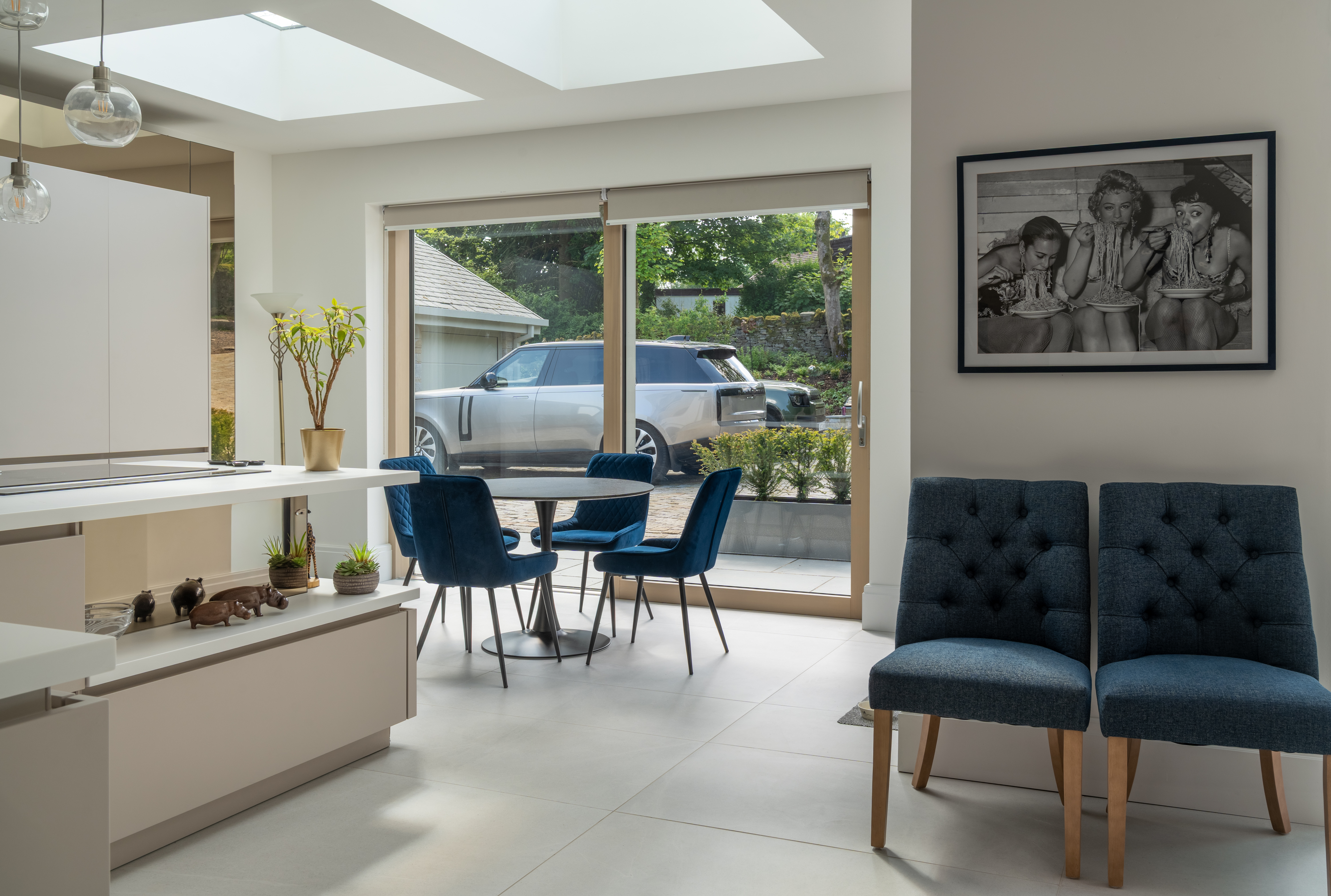 Open-plan kitchen-dining area with blue upholstered seating and bifold doors to the driveway