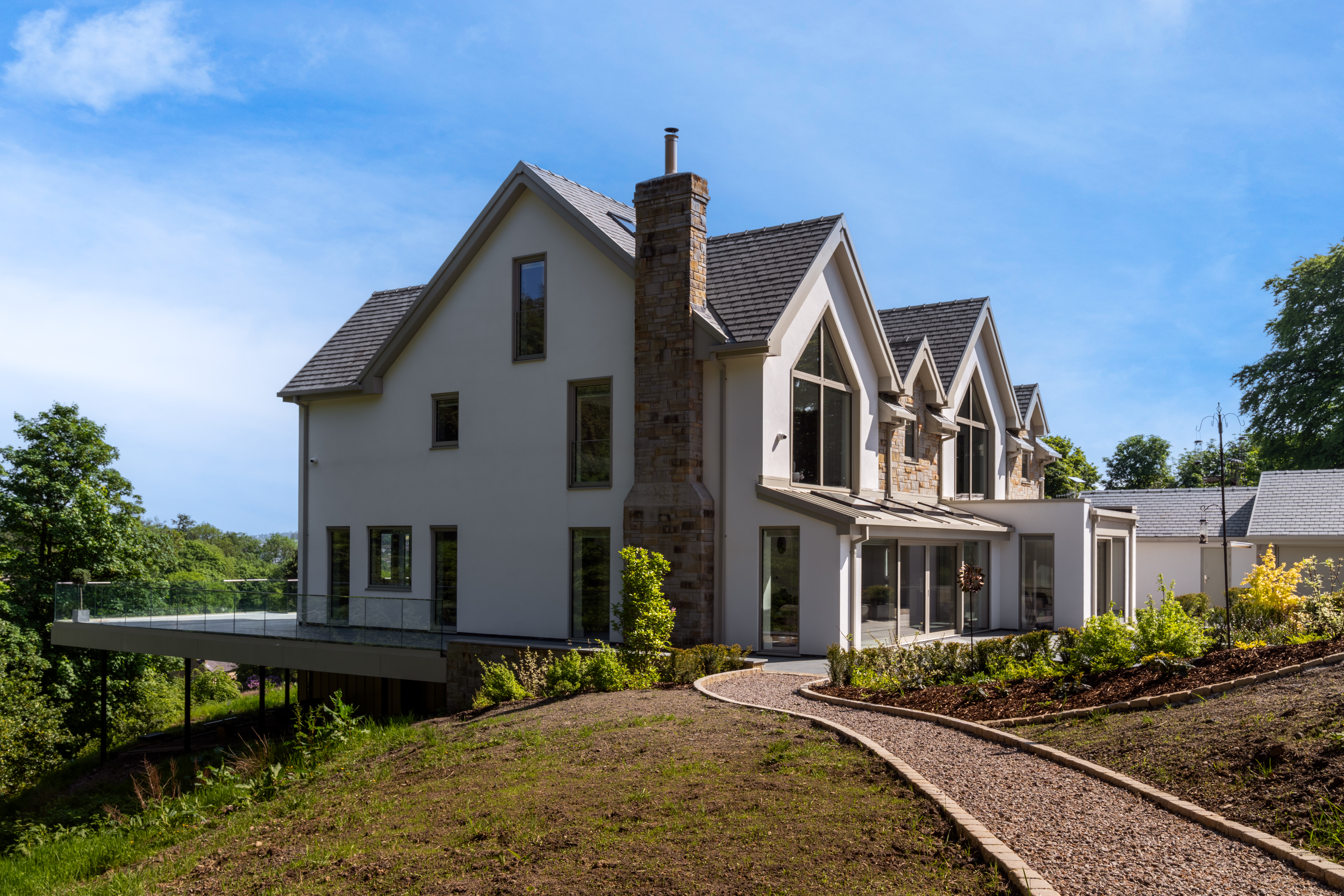Side exterior of a modern white render and stone house with pitched gables and landscaped garden